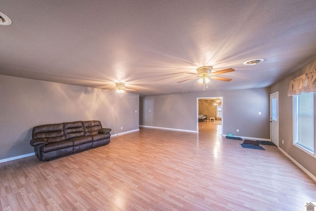 unfurnished living room with a ceiling fan, visible vents, baseboards, light wood-style flooring, and a textured ceiling