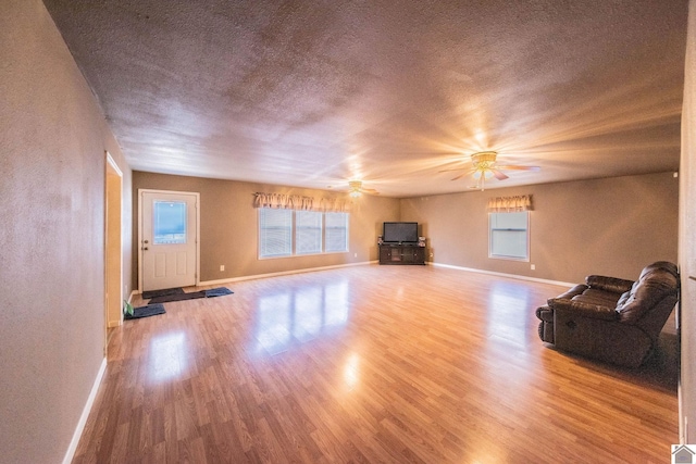 unfurnished living room featuring a ceiling fan, plenty of natural light, wood finished floors, and a textured ceiling