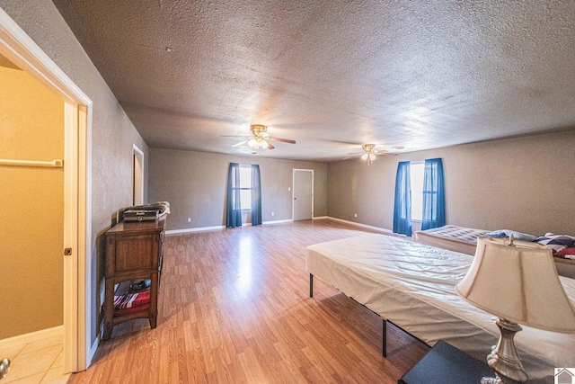 bedroom featuring multiple windows, a textured ceiling, baseboards, and light wood-style floors