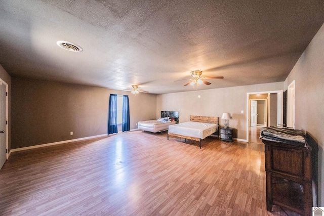 bedroom with visible vents, a textured ceiling, baseboards, and wood finished floors