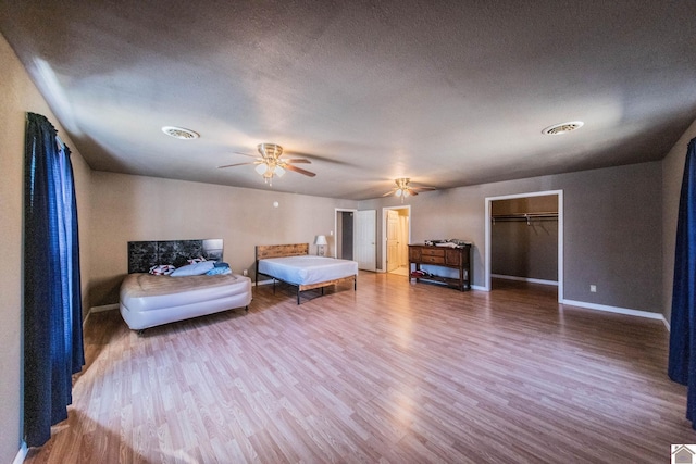 unfurnished bedroom featuring visible vents, a textured ceiling, wood finished floors, baseboards, and ceiling fan