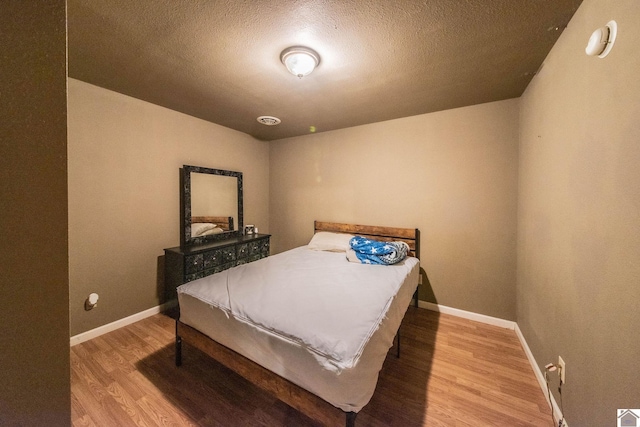 bedroom featuring baseboards, a textured ceiling, and wood finished floors