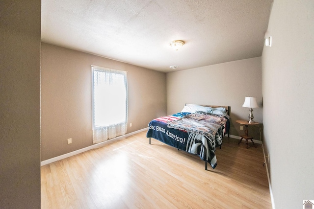 bedroom with wood finished floors, baseboards, and a textured ceiling