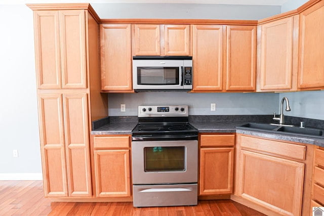 kitchen with dark countertops, light wood-style flooring, appliances with stainless steel finishes, and a sink