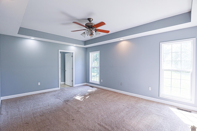 carpeted empty room featuring visible vents, a ceiling fan, a raised ceiling, and baseboards