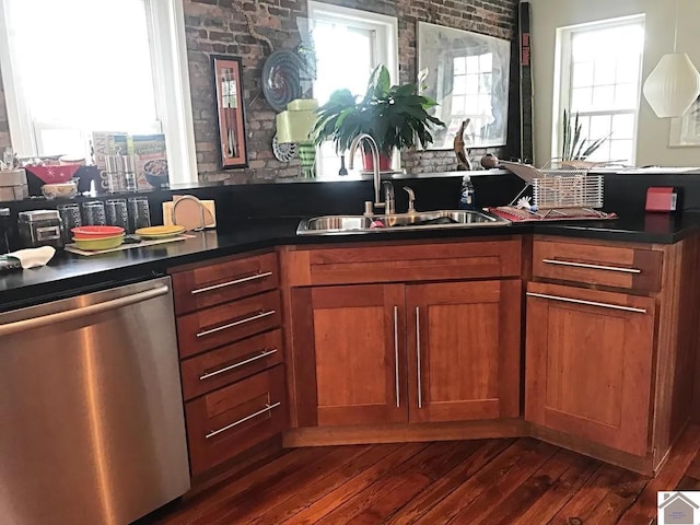kitchen with plenty of natural light, dark countertops, stainless steel dishwasher, a sink, and brown cabinetry