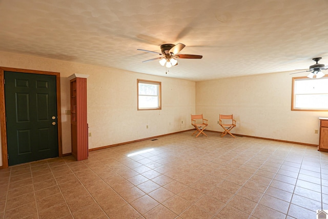 spare room featuring a textured ceiling, light tile patterned floors, baseboards, and ceiling fan