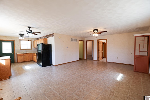 unfurnished living room featuring a sink, visible vents, baseboards, and a ceiling fan