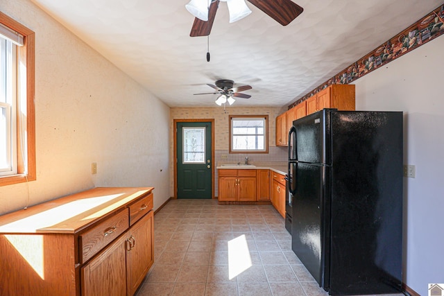 kitchen with light tile patterned floors, brown cabinetry, freestanding refrigerator, a sink, and light countertops