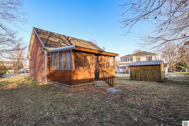 rear view of house with brick siding, an outdoor structure, a storage shed, and a sunroom