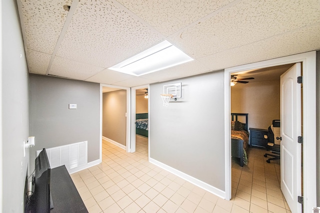 corridor featuring light tile patterned floors, visible vents, baseboards, and a drop ceiling