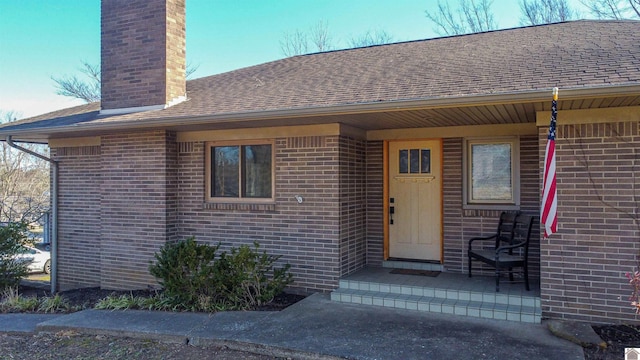 entrance to property with brick siding, a chimney, and roof with shingles