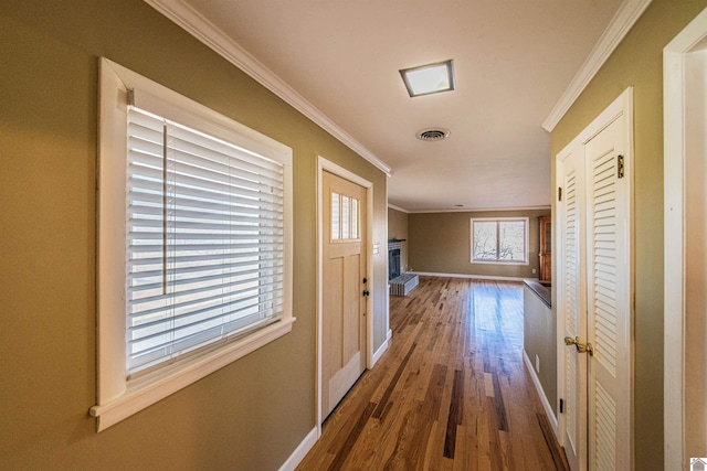 hallway with baseboards, wood finished floors, visible vents, and ornamental molding