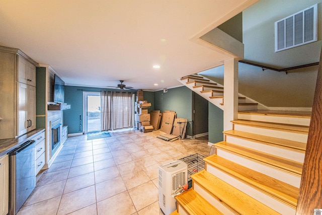 interior space with visible vents, a ceiling fan, stainless steel dishwasher, a glass covered fireplace, and light tile patterned flooring