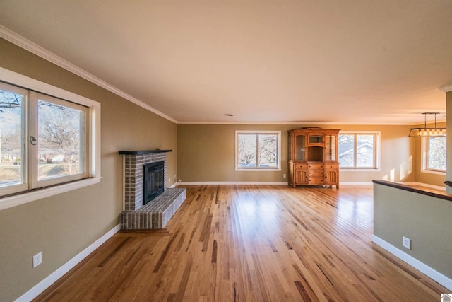 unfurnished living room with light wood finished floors, a glass covered fireplace, crown molding, and baseboards