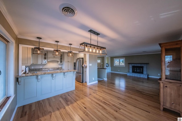 kitchen with light wood-type flooring, visible vents, freestanding refrigerator, a peninsula, and glass insert cabinets