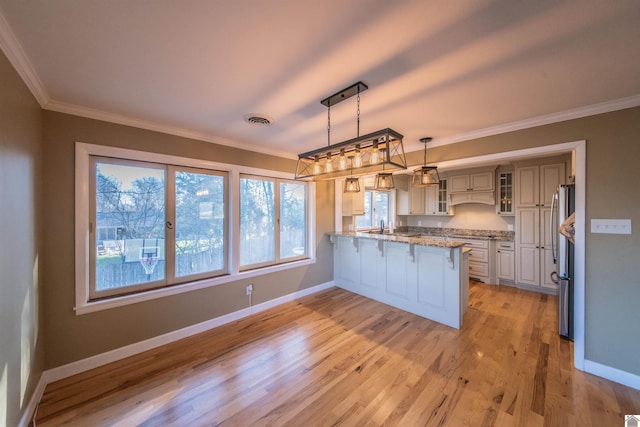 kitchen with visible vents, crown molding, a kitchen bar, a peninsula, and freestanding refrigerator