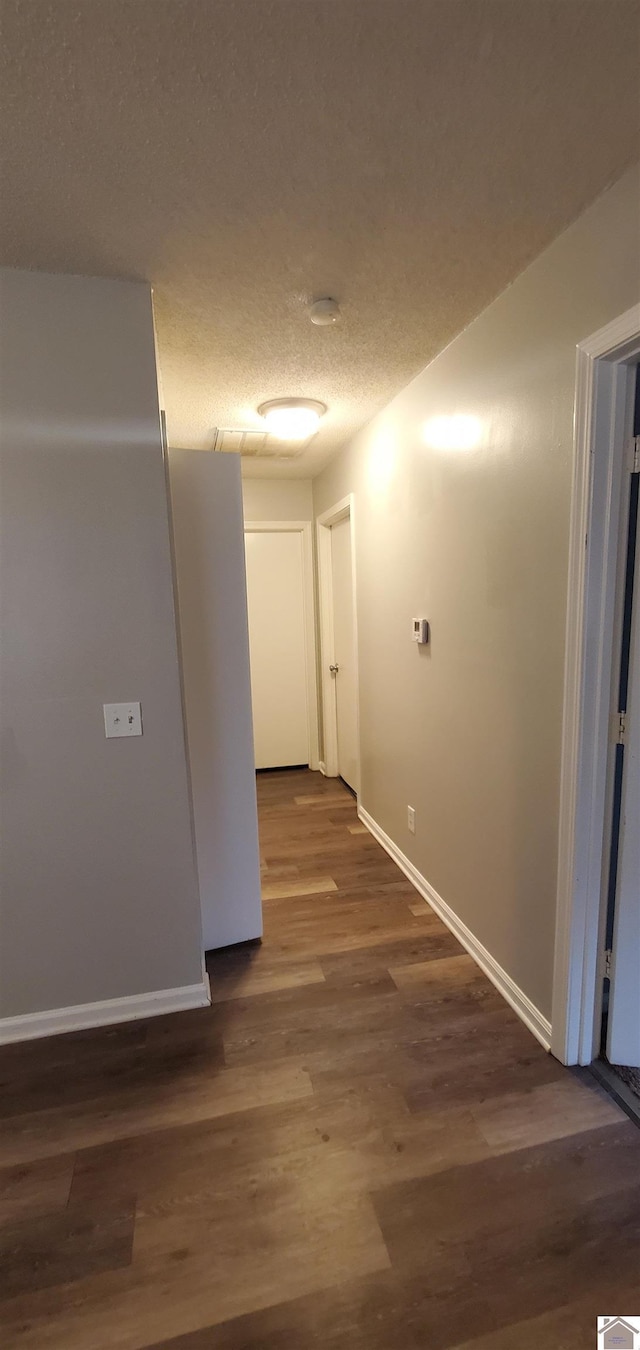 corridor featuring baseboards, dark wood-type flooring, and a textured ceiling