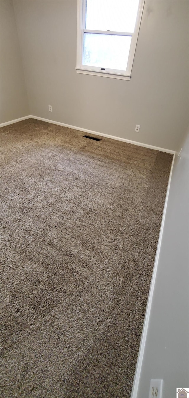 empty room with carpet, visible vents, and baseboards