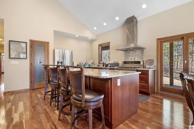 kitchen featuring appliances with stainless steel finishes, a center island, light wood-style floors, and wall chimney range hood