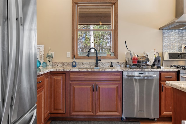 kitchen with a sink, wall chimney exhaust hood, light stone countertops, and stainless steel appliances