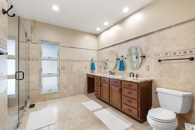 full bath with toilet, a sink, tile walls, a shower stall, and double vanity