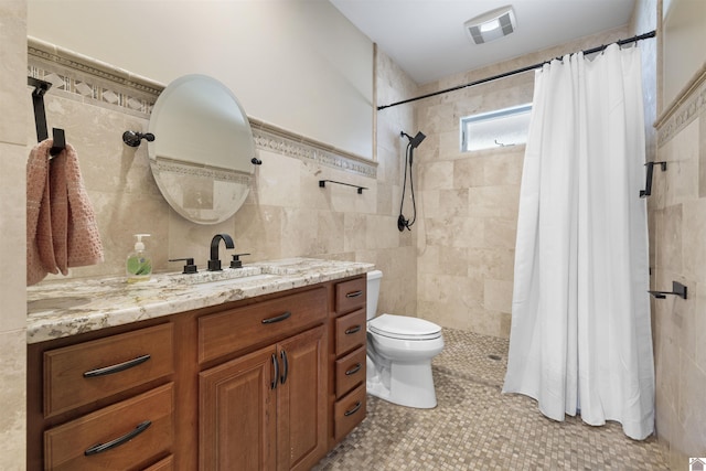 full bathroom with visible vents, toilet, vanity, tiled shower, and tile walls