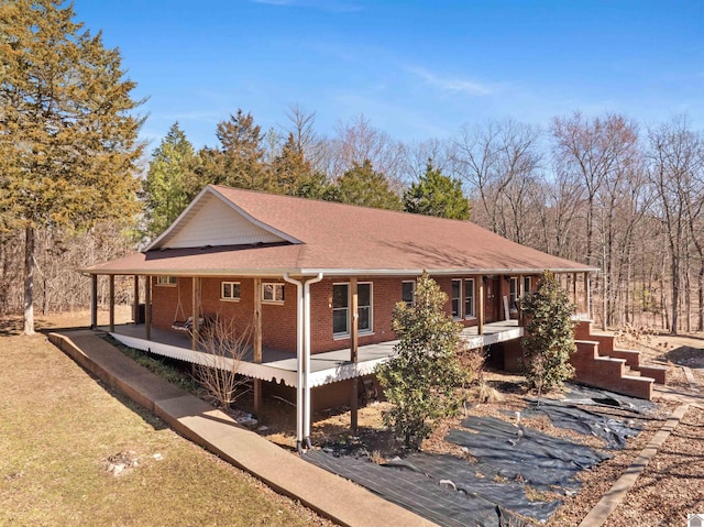 exterior space featuring a porch, a yard, brick siding, and a shingled roof