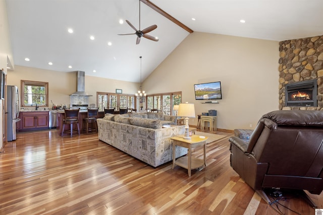 living room with beamed ceiling, ceiling fan with notable chandelier, a fireplace, light wood-style floors, and high vaulted ceiling