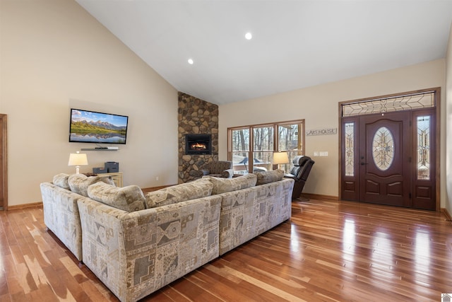 living room featuring light wood finished floors, baseboards, a stone fireplace, recessed lighting, and high vaulted ceiling