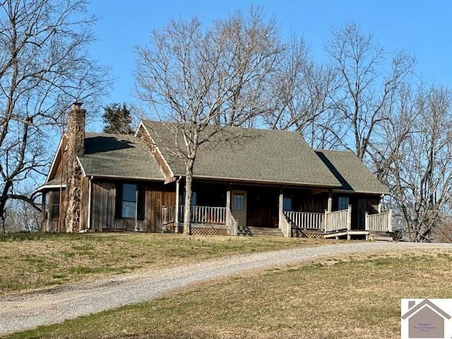 view of front facade with a chimney, dirt driveway, a porch, and a front yard