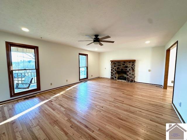 unfurnished living room featuring light wood-style flooring, a textured ceiling, recessed lighting, a stone fireplace, and ceiling fan