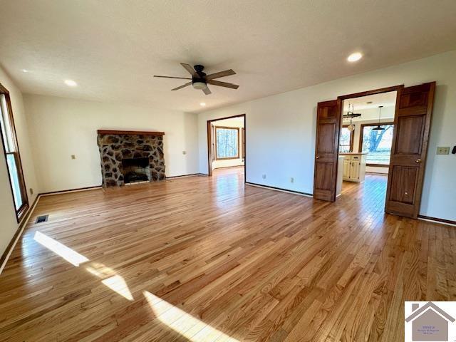 unfurnished living room featuring a stone fireplace, light wood-style flooring, plenty of natural light, and visible vents