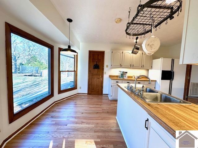 kitchen with freestanding refrigerator, a sink, light wood-style floors, pendant lighting, and white cabinetry