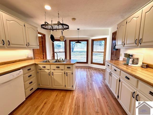 kitchen featuring a peninsula, light wood-style flooring, white dishwasher, butcher block countertops, and a sink