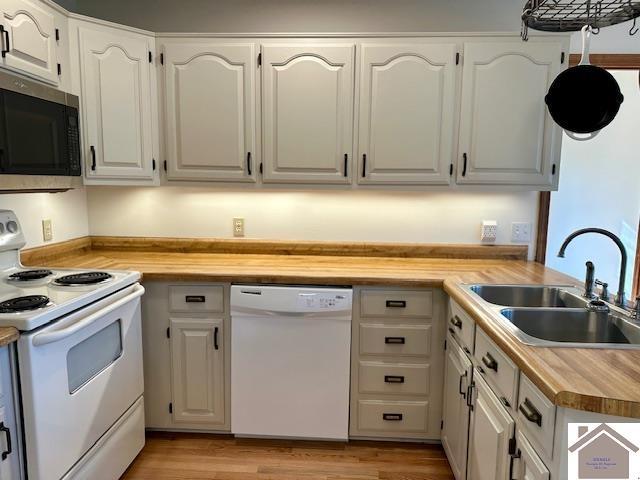 kitchen with a sink, wood counters, white appliances, white cabinets, and light wood finished floors