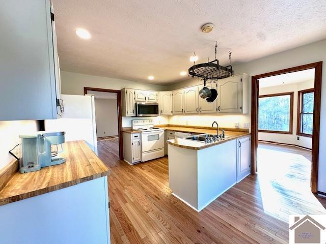 kitchen with white appliances, a peninsula, a sink, light wood-style floors, and a textured ceiling