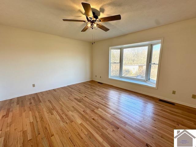 empty room with a ceiling fan, visible vents, light wood finished floors, and baseboards