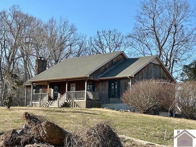 view of front of home with covered porch, a chimney, and a front yard