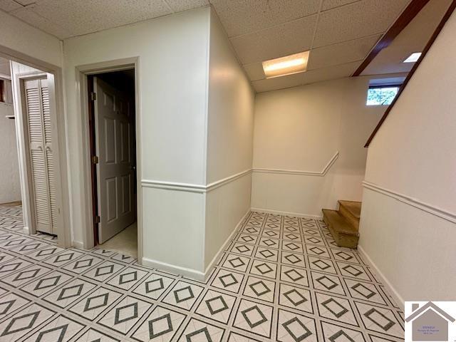 hall featuring stairs, a paneled ceiling, and baseboards