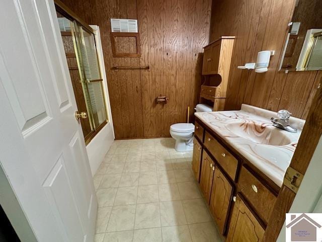 bathroom with vanity, toilet, wooden walls, and bath / shower combo with glass door