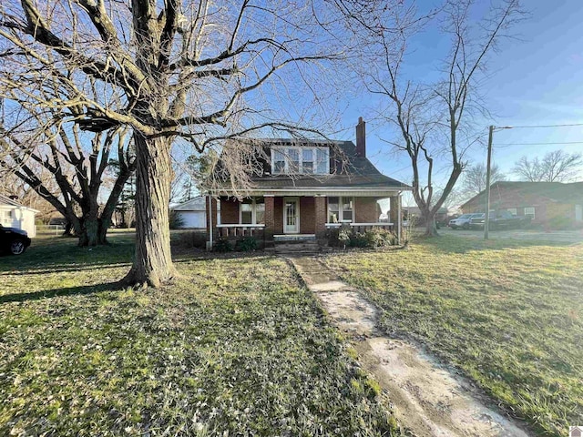 view of front of house featuring a front yard, brick siding, covered porch, and a chimney