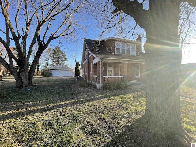 view of side of home featuring brick siding, a porch, a chimney, and an outbuilding