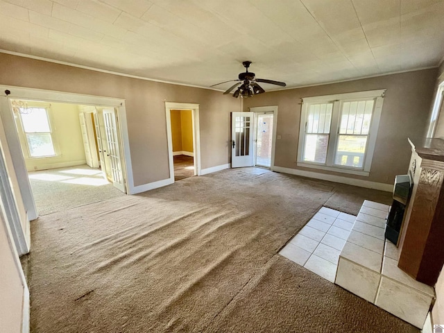 unfurnished living room featuring light carpet, baseboards, crown molding, and a ceiling fan