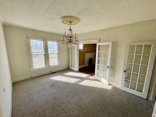 carpeted spare room featuring french doors, baseboards, an inviting chandelier, and crown molding