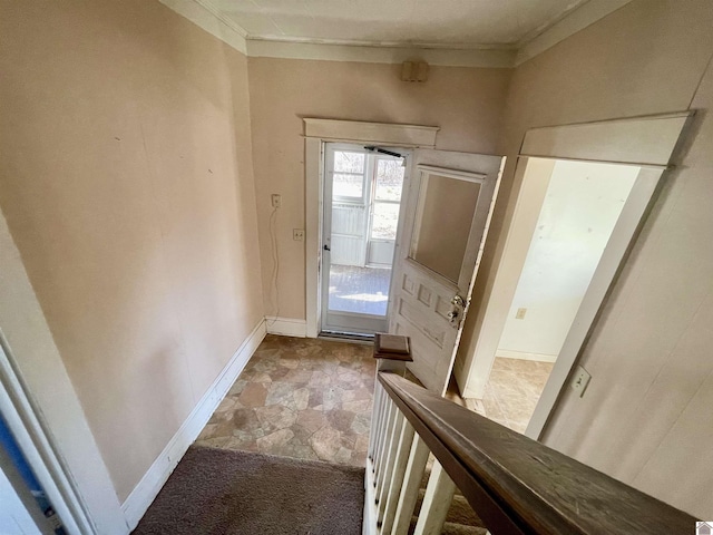 doorway with crown molding, stone finish floor, and baseboards