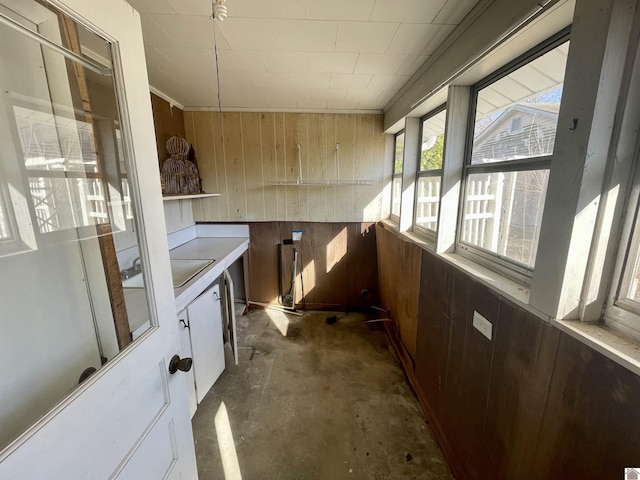 kitchen featuring unfinished concrete flooring, wood walls, light countertops, white cabinetry, and a sink