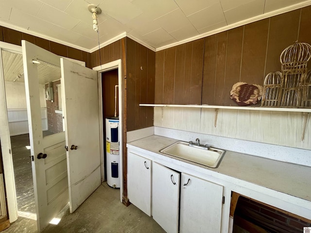 kitchen featuring water heater, a sink, light countertops, wood walls, and crown molding