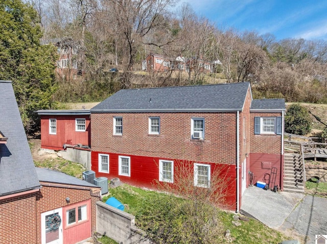 exterior space featuring brick siding, central AC, and roof with shingles