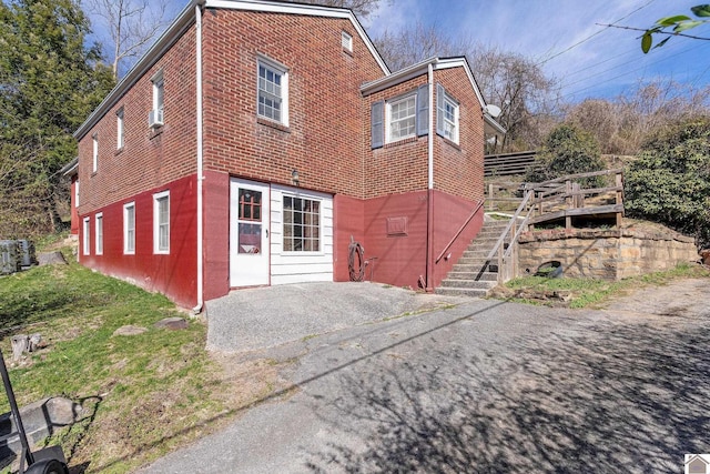 rear view of property with stairway, a deck, aphalt driveway, a patio area, and brick siding